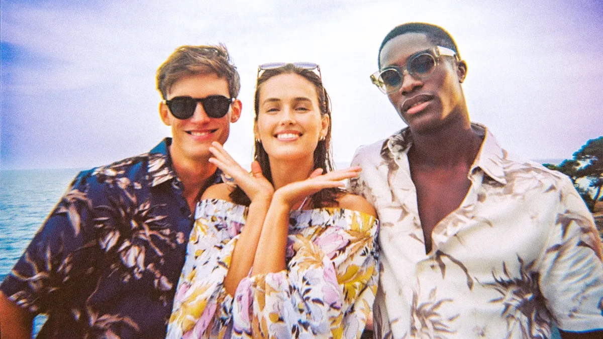 Three people in patterned shirts smile at the camera.