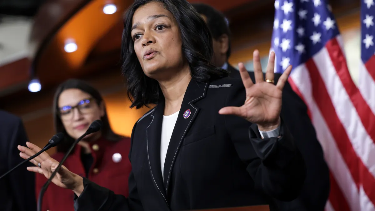 Rep. Pramila Jayapal speaks at a podium with an American flag behind her.