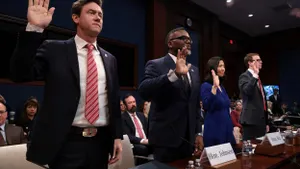 Three people wearing dark suits and one person wearing a blue dress stand with their hands raised.