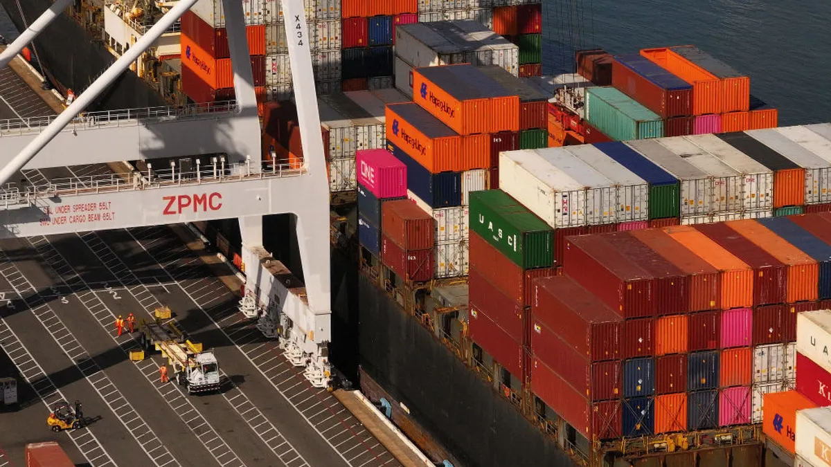 In an aerial view of a shipping container is loaded onto a truck on a dock at an ocean port in California.