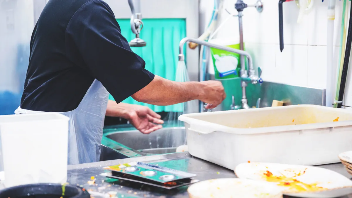 A person handles dirty dishes at an industrial sink.