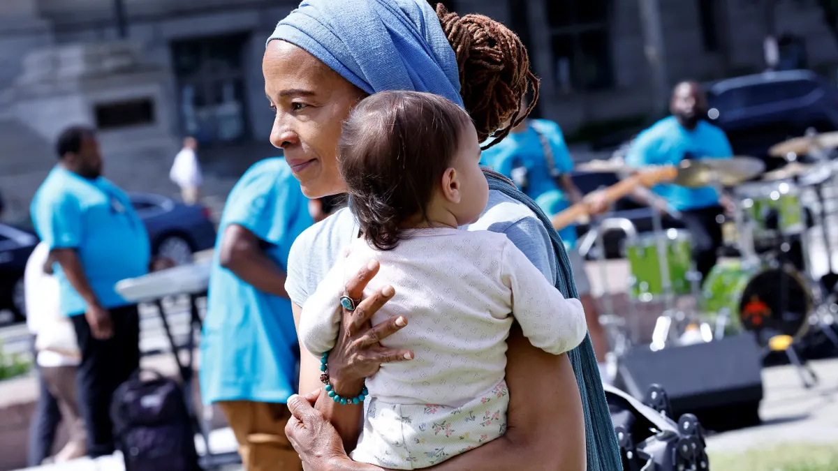 A person holds a baby at an outdoor rally.