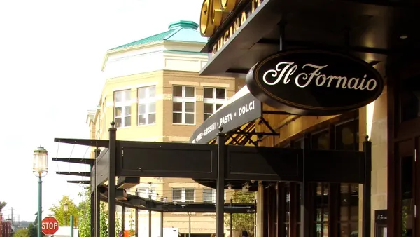 A view from the sidewalk of an outdoor seating area on a city corner with an "Il Fornaio" sign above it.