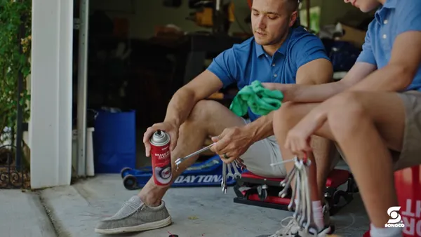 An adult uses an aerosol can containing cleaner while working on auto parts with a child.