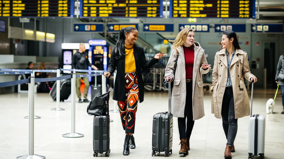 Three people with walking through the airport with their role on luggage.