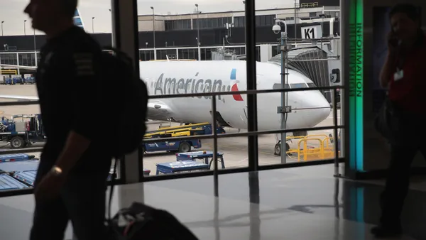 A passenger walks in an airport terminal. An American Airlines plane can be seen through the window.