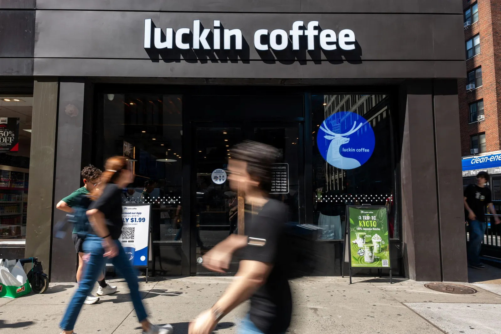 People walk by a coffee shop with a white sign that says "Luckin Coffee"