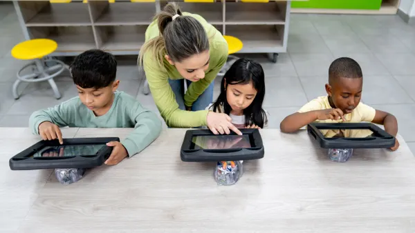 A teacher guides three young students using tablets in a classroom.