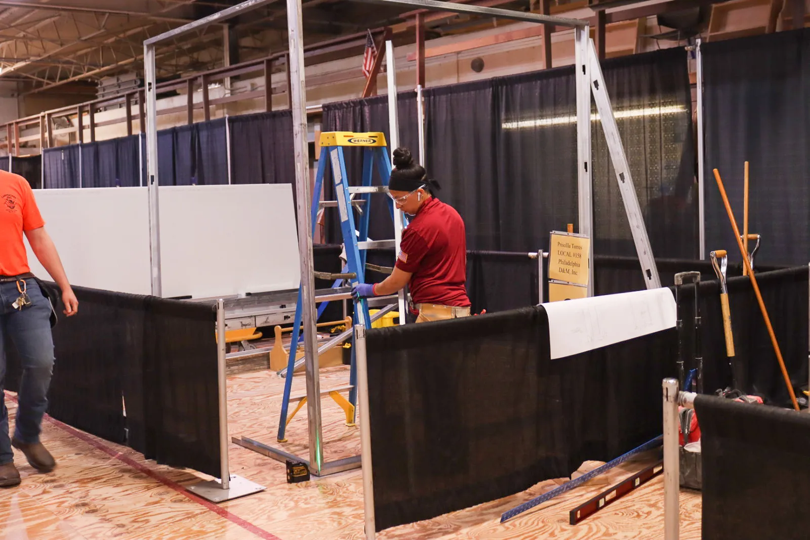 A carpenter in a red shirt adjusts a letter inside of a curtained off booth.