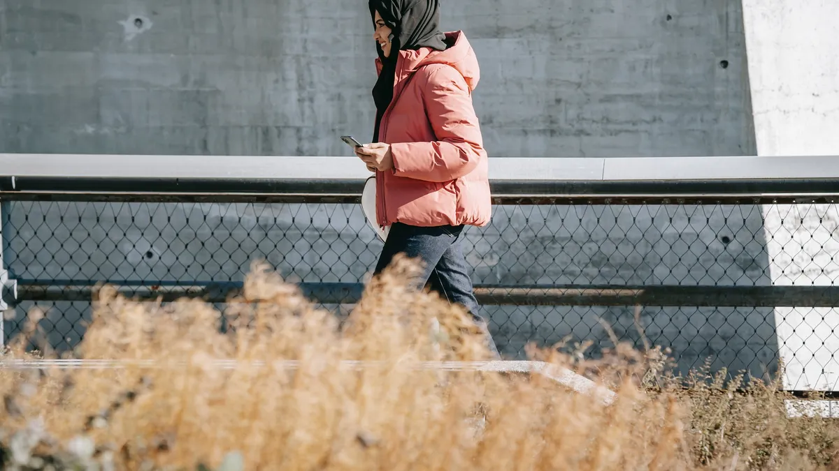 college students walks across campus holding a cell phone