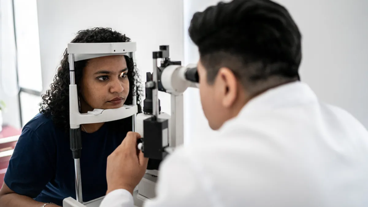 A doctor examines a patient's eyes using a light and a microscope.