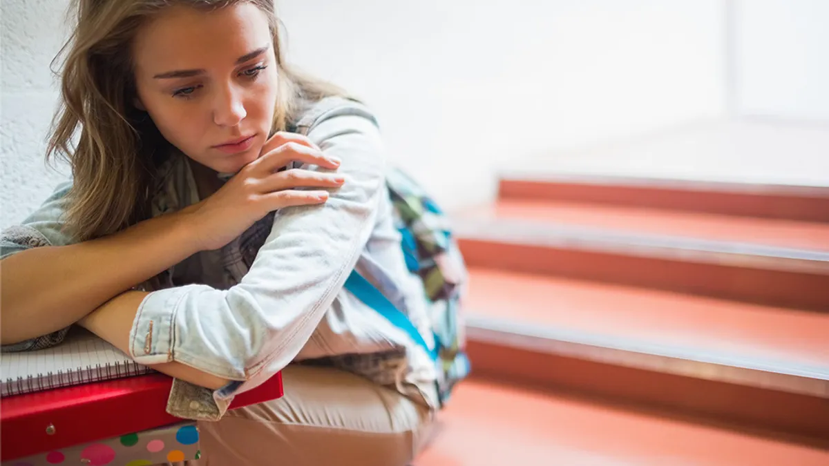 Student sitting on school stairway in thought with books