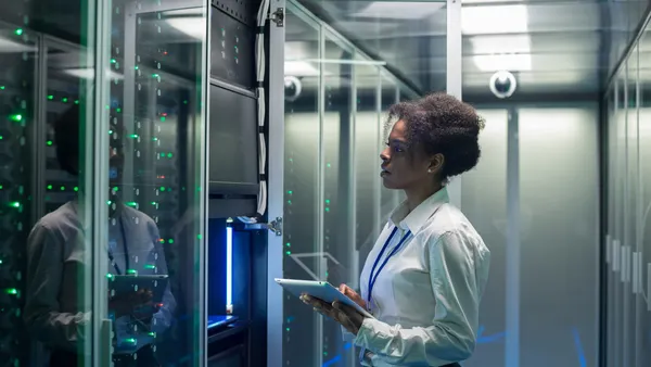 female technician working on a tablet in a data center full of rack servers