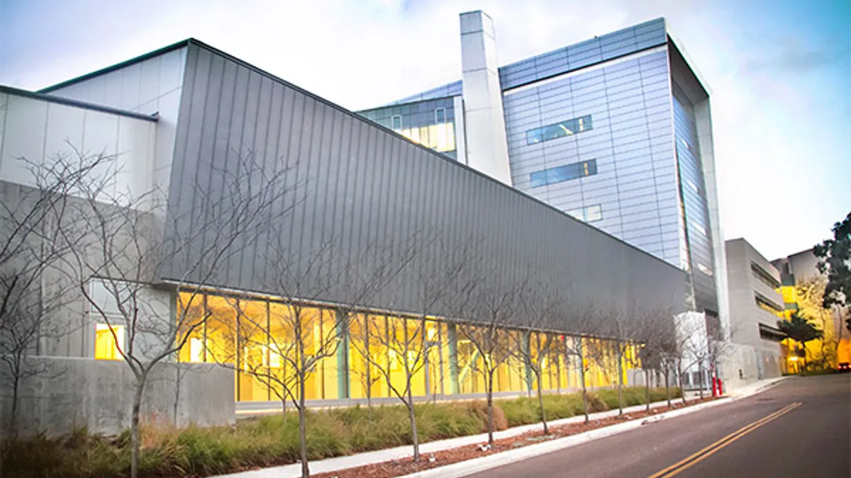 A shot of a building's exterior along a paved road. The modern looking building, covered in glass, looms in the photo.