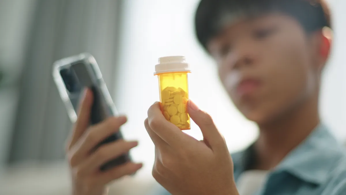 young man holds smart phone and looks at orange bottle of pills blurred