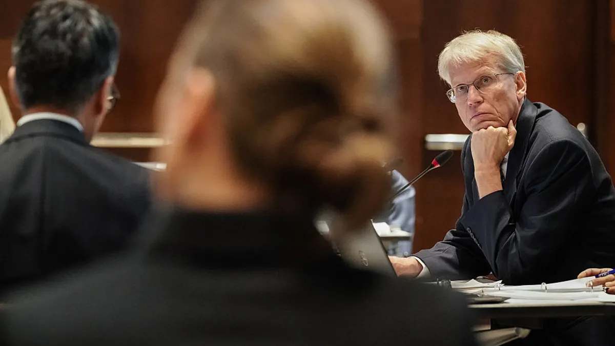 A person in a business suit listens to a presentation while sitting at a desk.