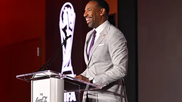 A person wearing a suit speaks at a podium with a sign that says "The Coca-Cola Company"