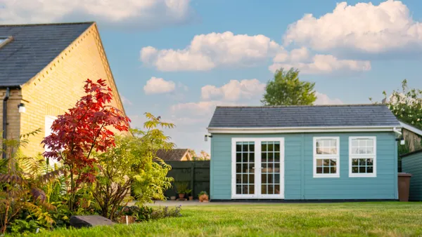 A small blue house sits next to a larger yellow house in a  yard.