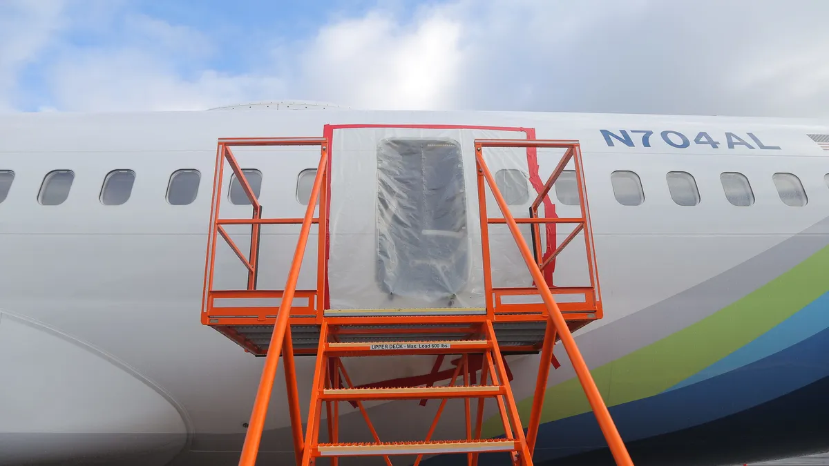 An orange mobile staircase facing the door hole covered in plastic on an aircraft.