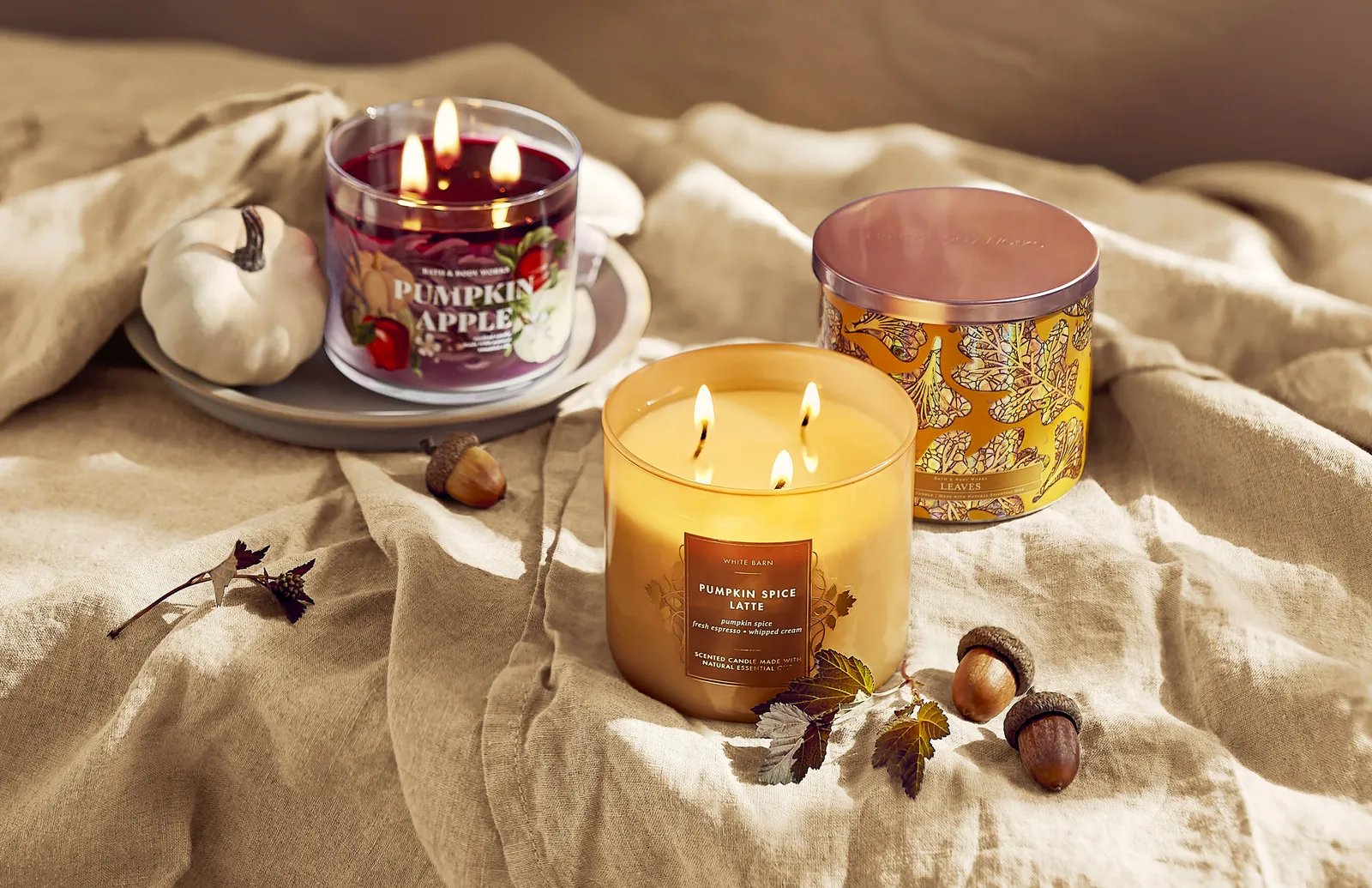 A display of three Bath & Body Works fall candles in various scents and colors