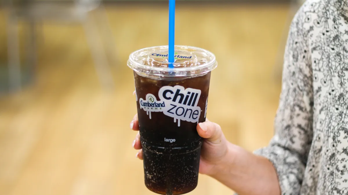 A photo of a hand holding a disposable clear cup with soda inside and a straw through the lid. The cup says Cumberland Farms Chill Zone.