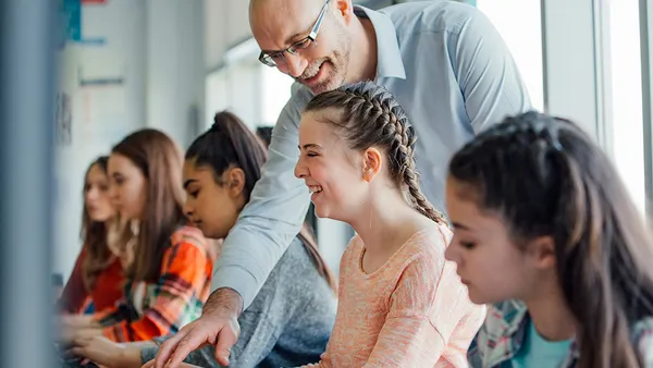 A teacher helping a student on the computer and smiling
