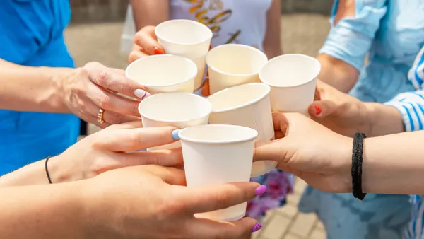 Seven people's hands holding paper cups come together for a toast.