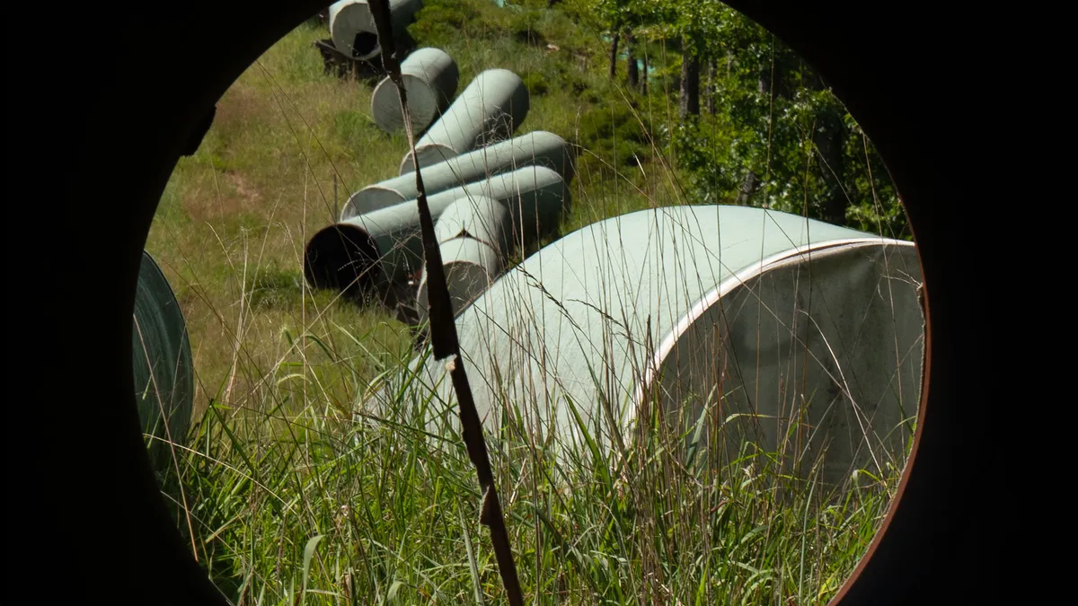 Sections of large grey pipes for the Mountain Valley Pipeline rest in tall grass.