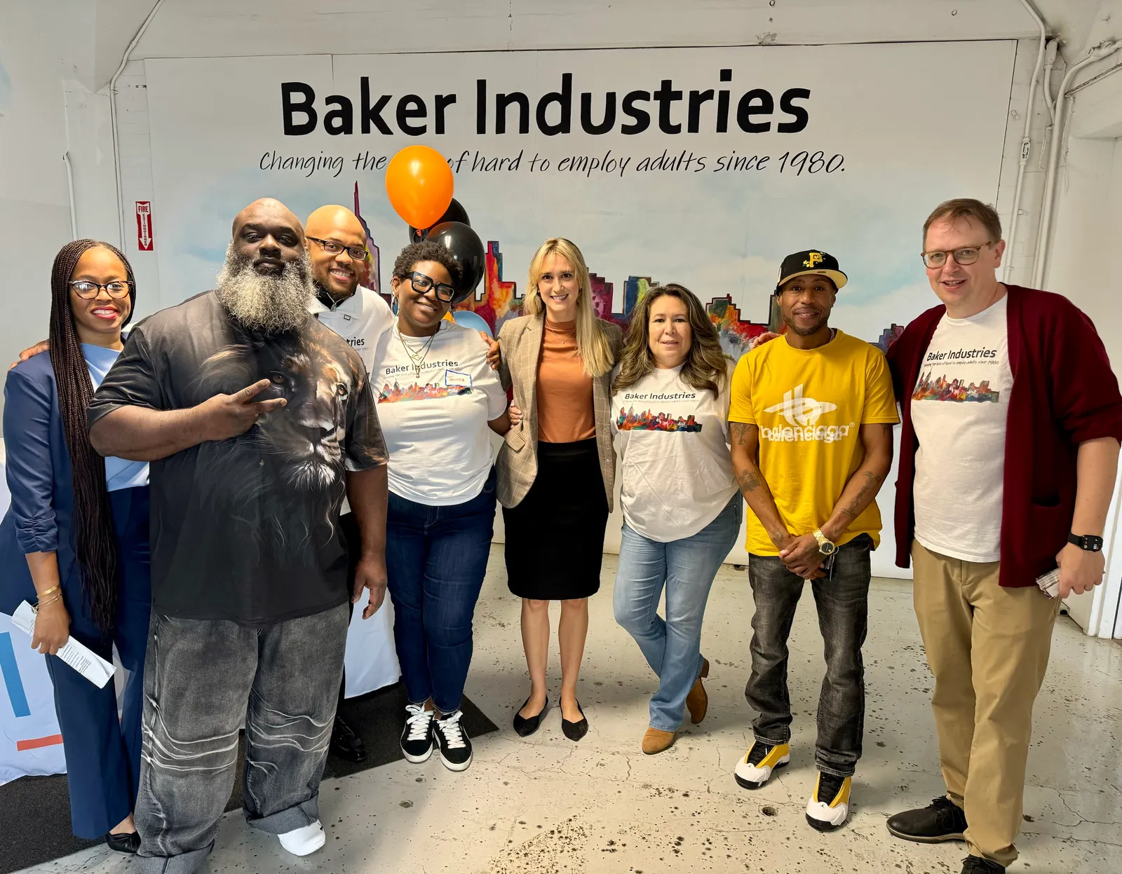 Baker Industries participants pose in front of a sign that says "Changing the life hard to employ adults since 1980"