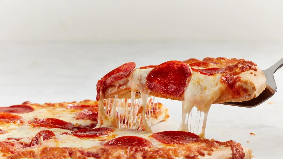 A photo of a pizza on a white background, with one slice being pulled up and away.