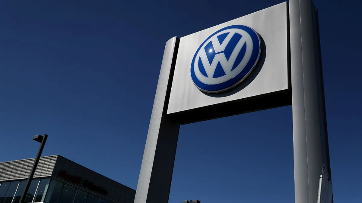 A Volkswagen sign jets out into the blue sky as a dealership building is seen in the lower-left corner of the image.