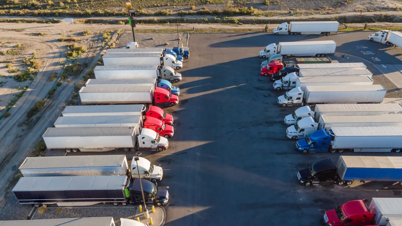 Tractor-trailers parked in a lot next to roadways.