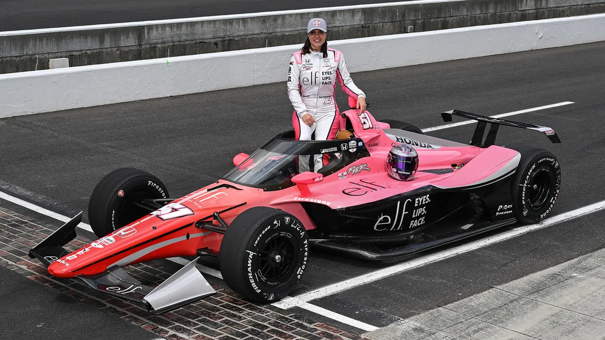 Professional race car driver Katherine Legge is seen standing on a race track next to an E.l.f. Cosmetics-branded car while also wearing E.l.f.-branded gear for the Indy 500.