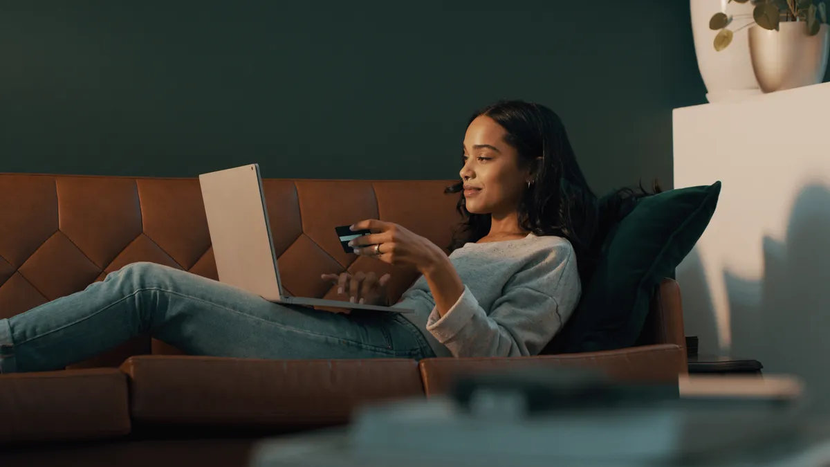 Person laying back on a couch with a computer and a credit card shopping.