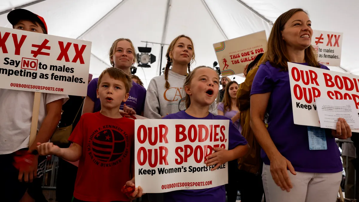 Parents and children hold signs protesting transgender rights in athletics