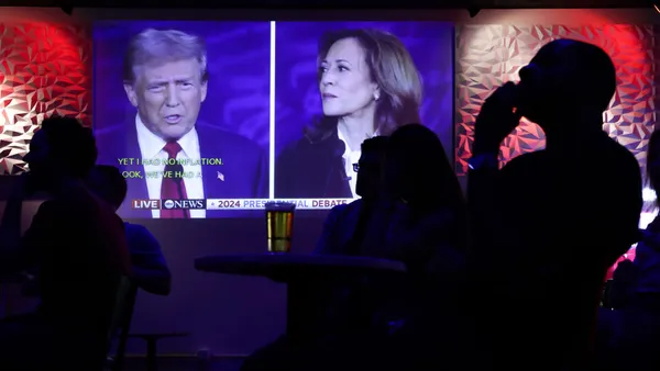 People in a bar watch a TV screen with former President Donald Trump and Vice President Kamala Harrris debating.