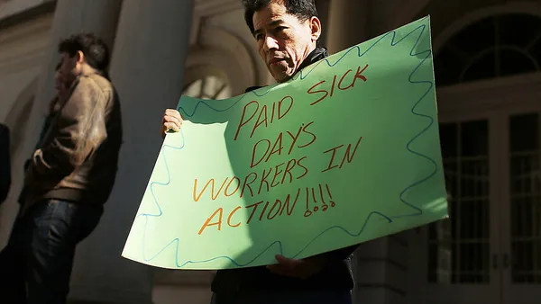 Man holds sign stating "Paid sick days workers in action" during rally for paid sick leave bill