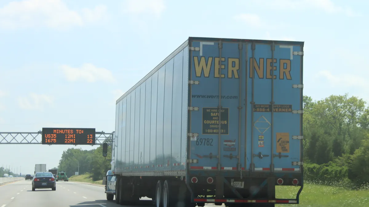 A Werner tractor-trailer on a highway alongside passenger traffic.