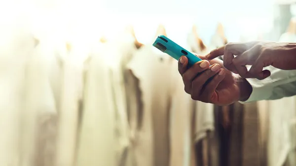 A person holds a mobile device while standing in a clothing store.