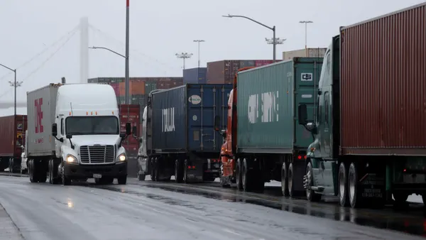 Trucks carrying shipping containers wait in line.