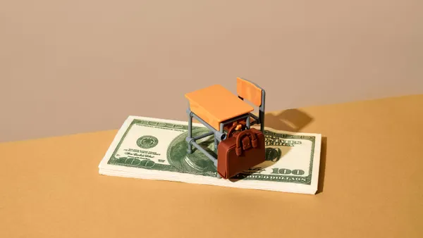 A toy school desk and chair stands on top of a stack of money.