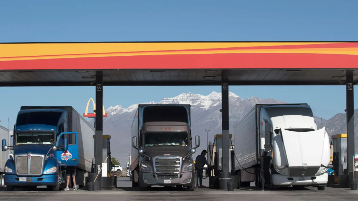 Truck drivers alongside their big rigs at a fuel station with a mountain range and McDonald's sign in the background.