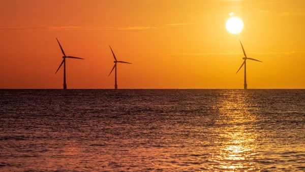 Offshore wind farm turbines silhouetted against an orange sunrise.