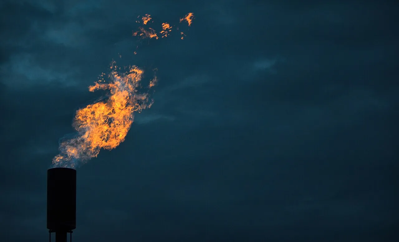 A flame burns out of a metal stack against a dark sky