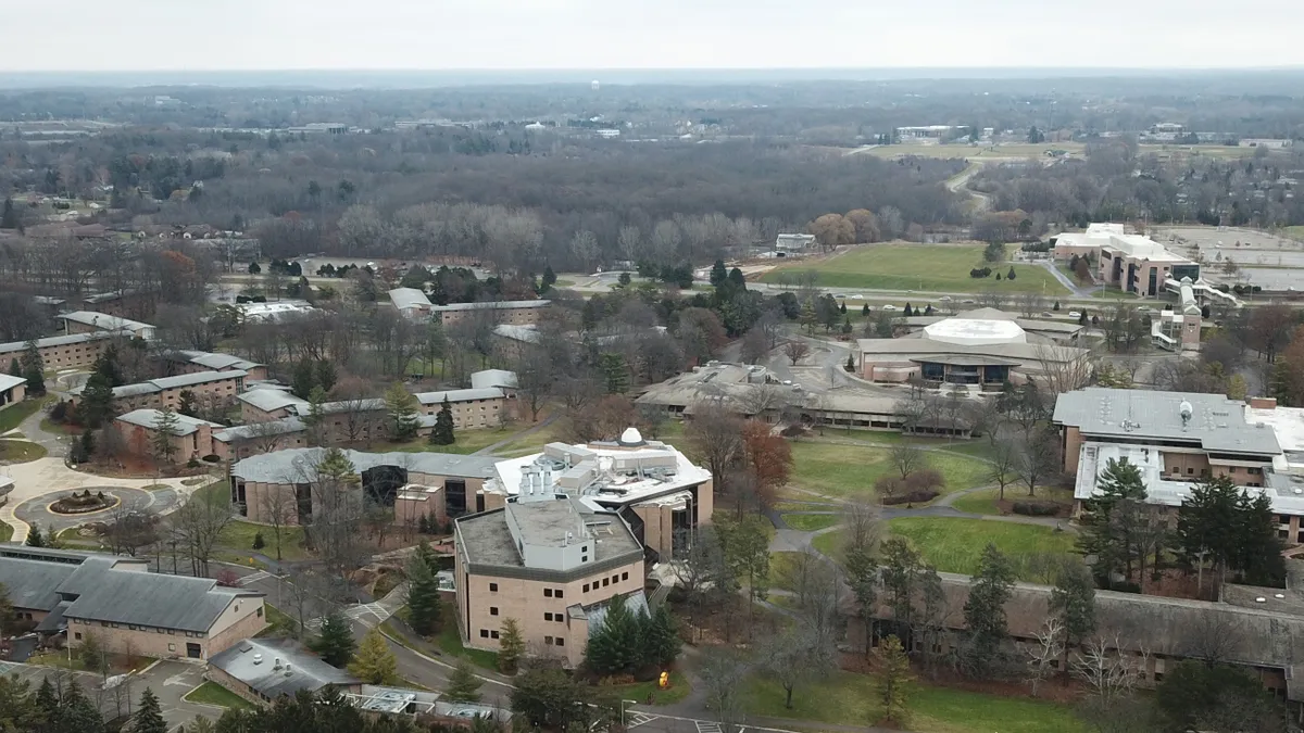 An aerial view of a college campus, with a mix of beige buildings and green open spaces