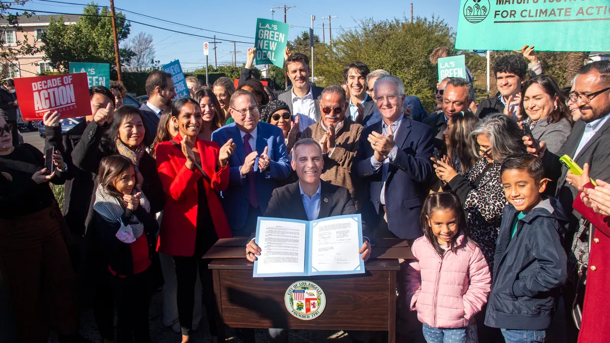 Man sitting at table, holding up a signed law, surrounded by a crowd of people