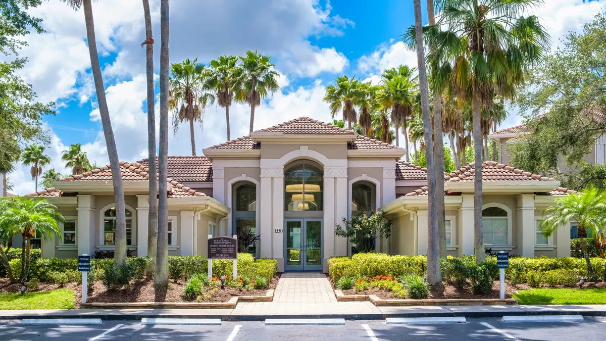 One story tan apartment entrance with palm tree in the foreground.