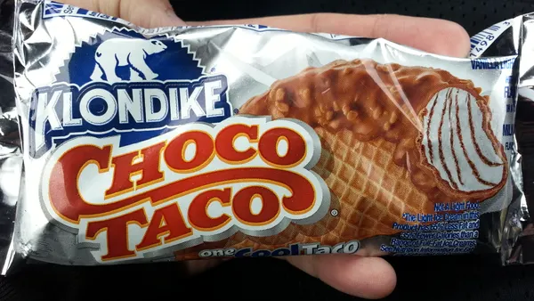 A person holds a silver-wrapped Choco Taco ice cream novelty