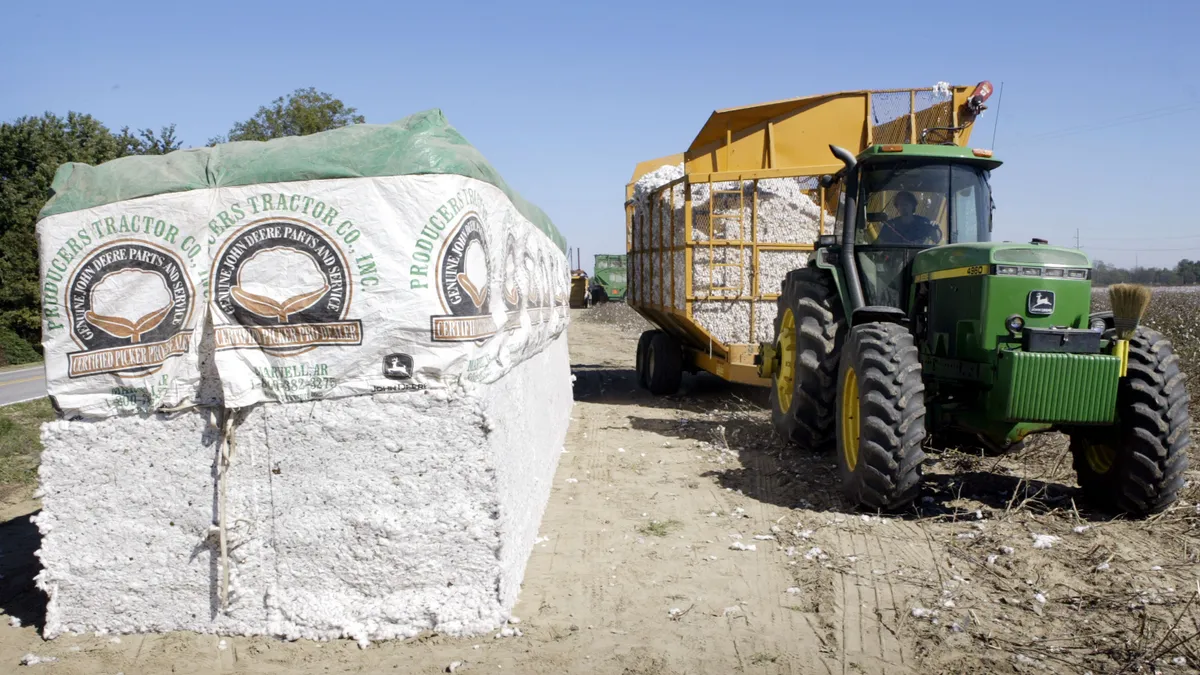 A person operates a tractor that is harvesting cotton on a farm.