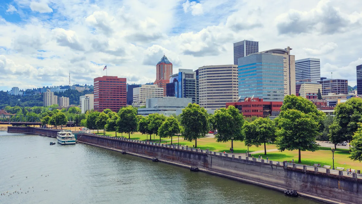 A city skyline behind a waterway lined by trees. A boat is in the waterway.